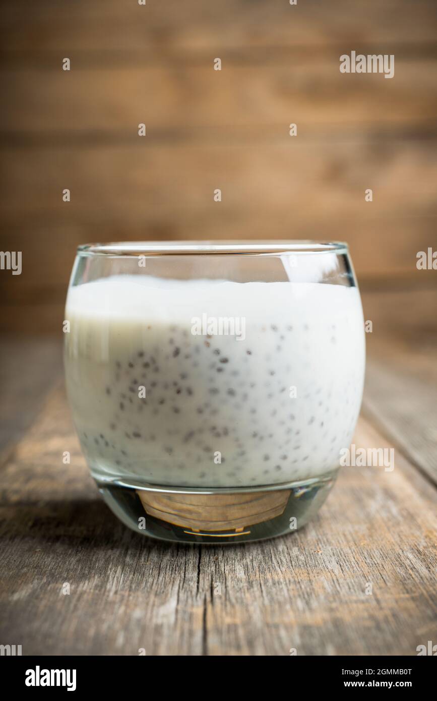 Yogurt semplice con semi di chia in vetro sullo sfondo rustico in legno. Messa a fuoco selettiva. Foto Stock
