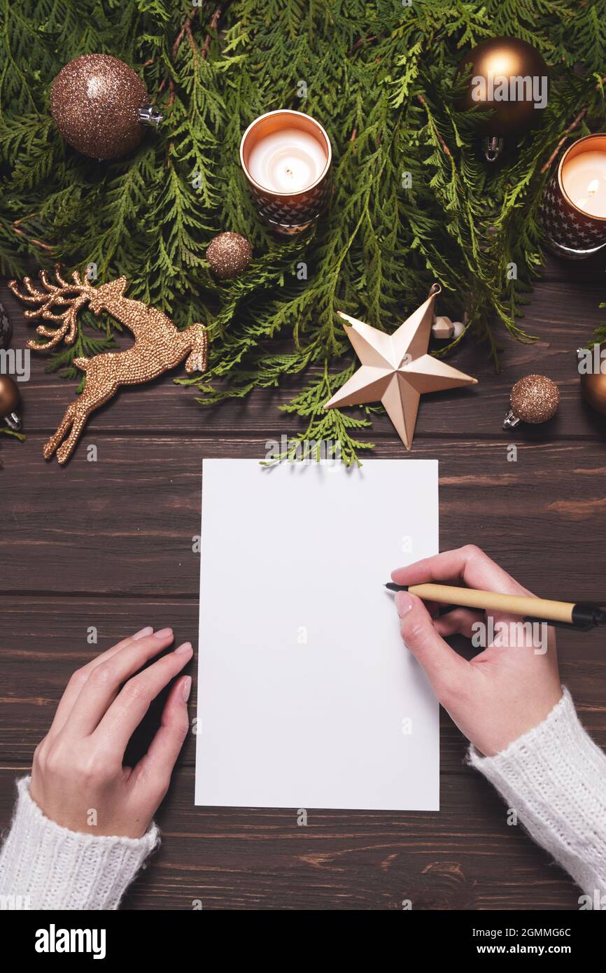 Le mani femminili scrivono la cartolina di Natale o la lista dei desideri su sfondo di legno. Foto Stock