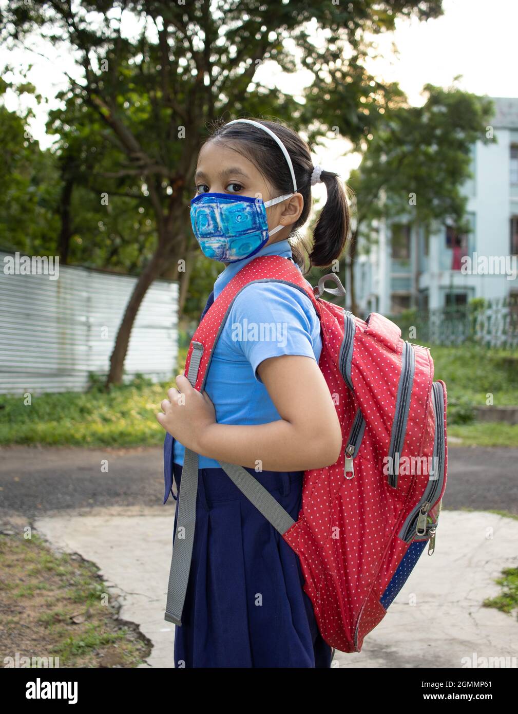 Ritratto di una ragazza indiana felice studente bambino in uniforme blu scuola con sacco rosso e maschera naso protezione andare a scuola Foto Stock