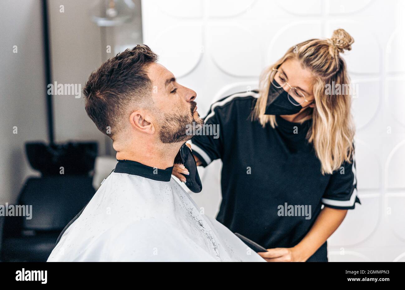 Parrucchiere con maschera rasando un uomo con una macchina elettrica Foto Stock