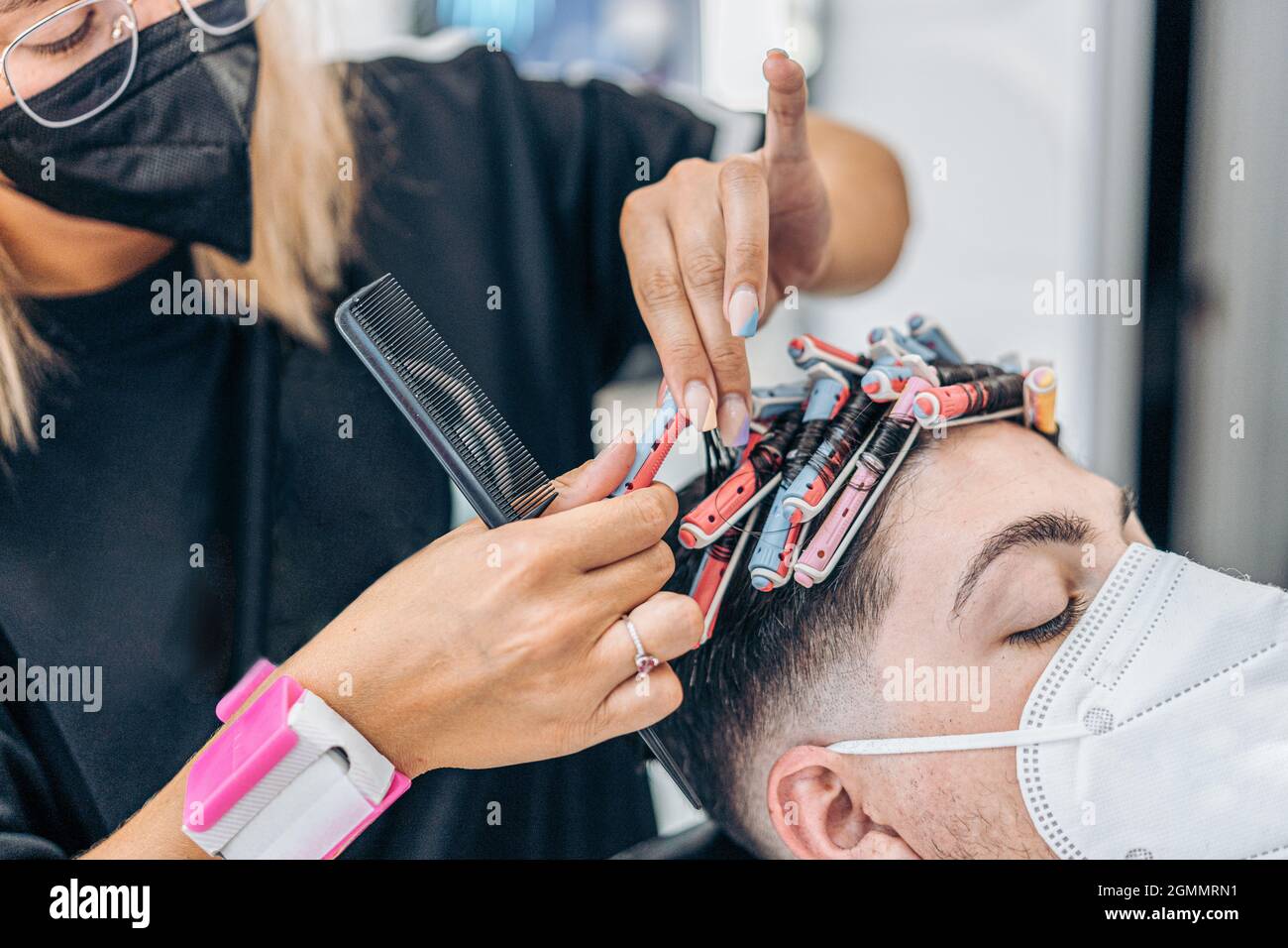 Vista ravvicinata di un parrucchiere che arriccia i capelli di un uomo utilizzando una maschera Foto Stock