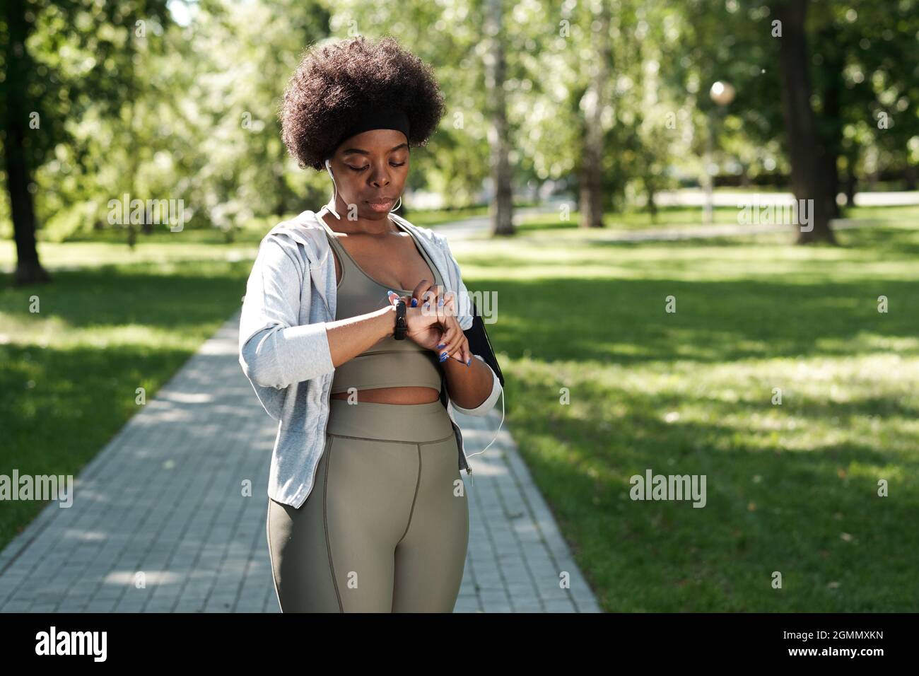 Giovane donna sportiva che guarda lo smartwatch al polso mentre è in piedi nel parco Foto Stock