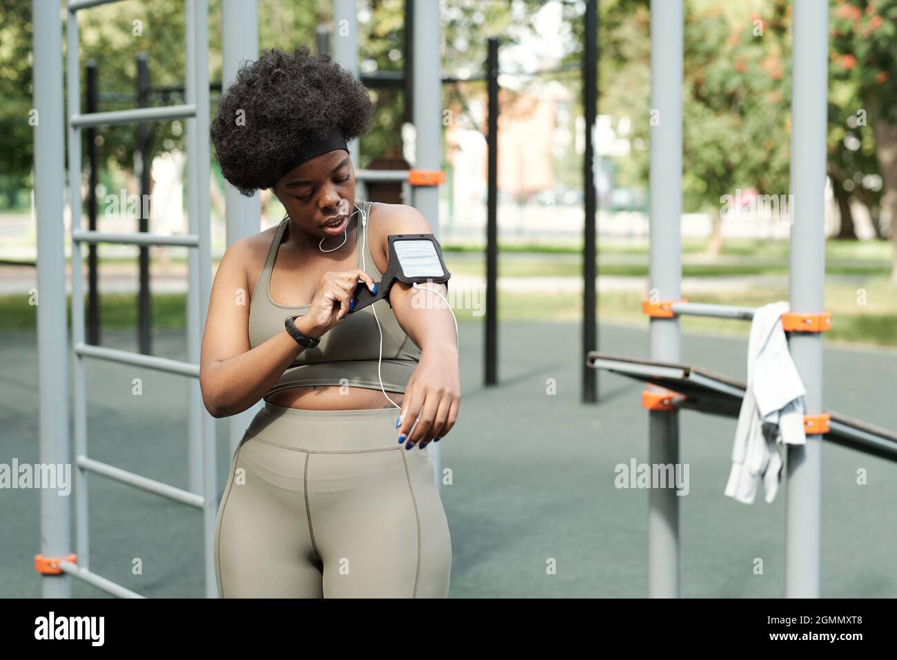 Giovane donna africana attiva fissando smartphone al suo braccio prima di allenarsi all'aperto Foto Stock