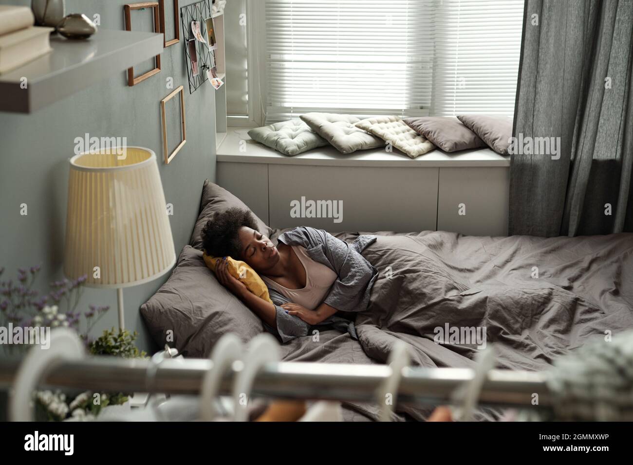 Giovane donna contemporanea di etnia africana che si trova nel letto all'interno di una camera da letto accogliente Foto Stock