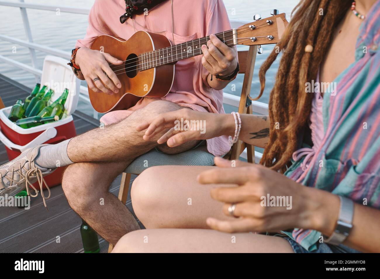 Mani di giovane uomo con chitarra e la sua ragazza che si rilassano sul molo il giorno d'estate Foto Stock