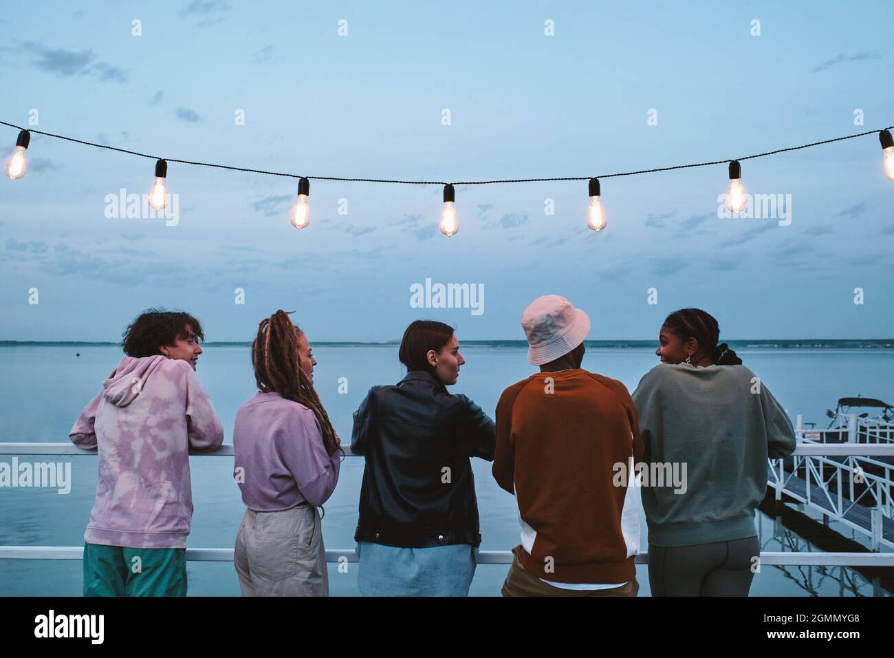 Gruppo di giovani amici che guardano la ragazza africana durante la conversazione in riva al mare la sera d'estate Foto Stock