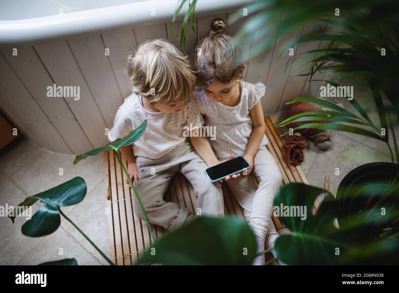 Vista dall'alto di bambini piccoli e carini seduti sul pavimento in bagno, utilizzando lo smartphone. Foto Stock