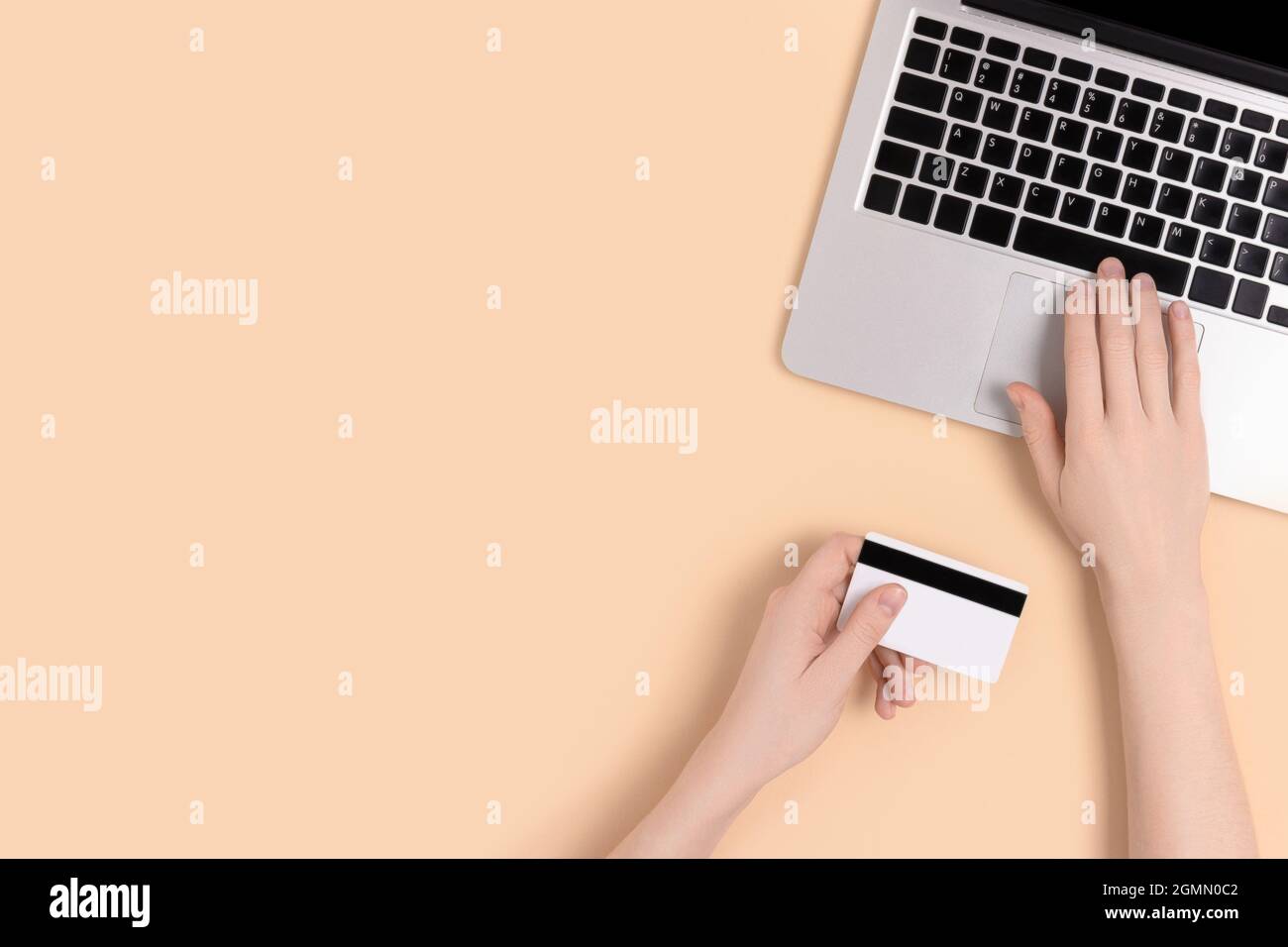 Le mani femminili che digitano sul laptop e tengono la carta di credito. Concetto di shopping online su sfondo beige. Foto Stock