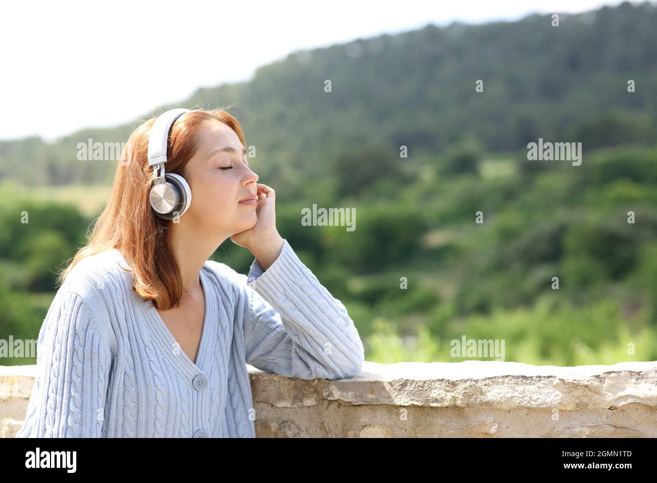 Donna che indossa cuffie senza fili che riposano ascoltando la musica in un balcone in una casa rurale Foto Stock