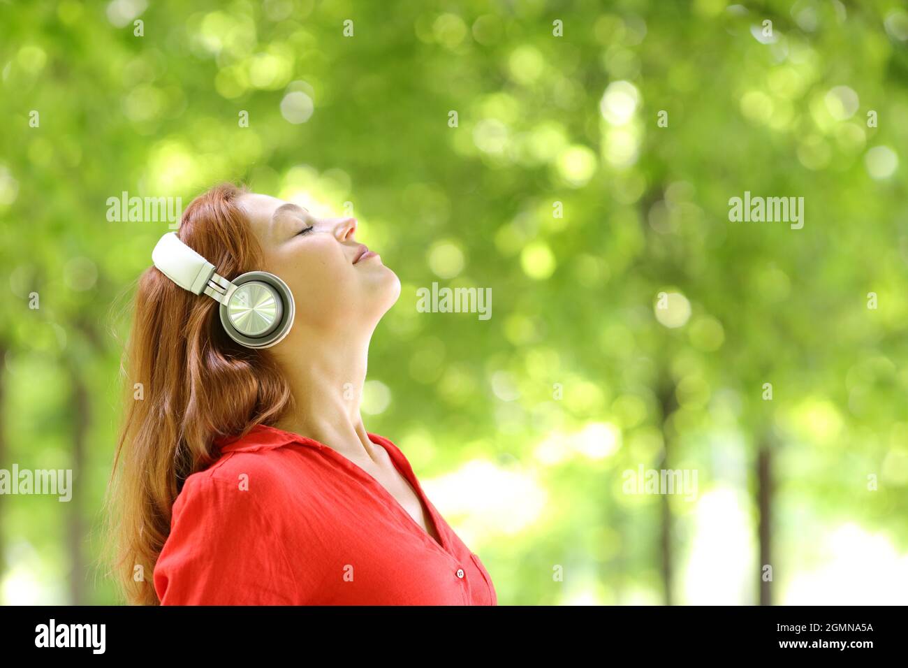 Ritratto della vista laterale di una donna che indossa cuffie wireless meditating in un parco verde Foto Stock