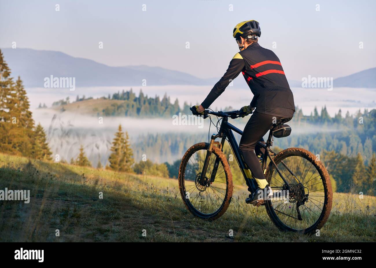 Vista posteriore del ciclista maschile in tuta da ciclismo in bicicletta su  strada. Uomo bicyclist indossare casco di sicurezza mentre si gode in  bicicletta in montagna al mattino. Concetto di sport, ciclismo