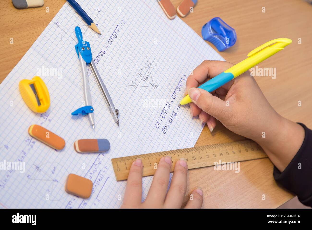 Primo piano della mano della pupilla risolvere un esempio di geometria in un notebook. Uno scolaro svolge un compito sul posto di lavoro. Il concetto di educazione dei bambini, di insegnamento delle conoscenze, delle competenze e delle abilità. Foto Stock