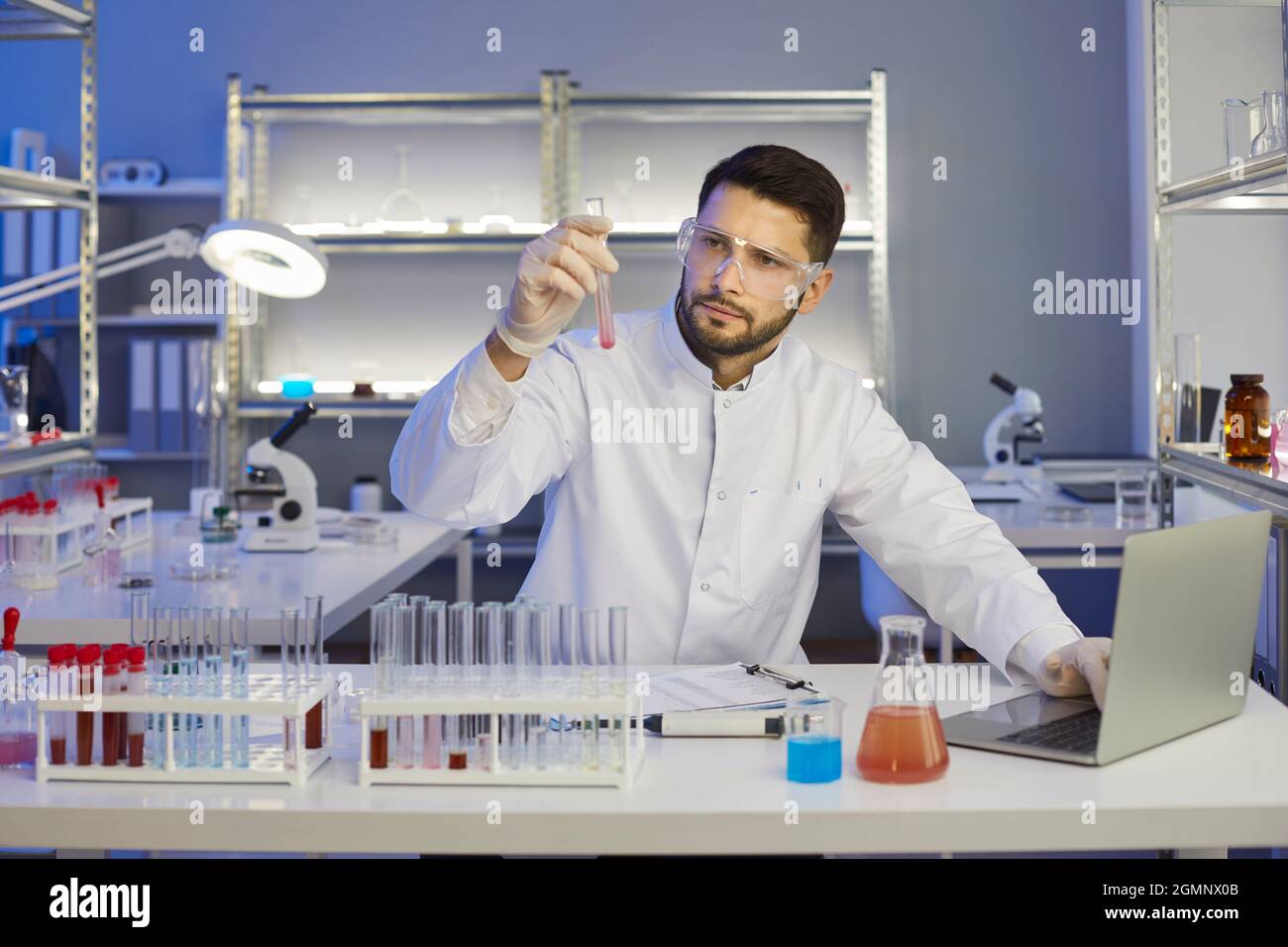 Uomo scienziato concentrato che guarda la provetta con campioni di sangue e fluido chimico in mano. Foto Stock