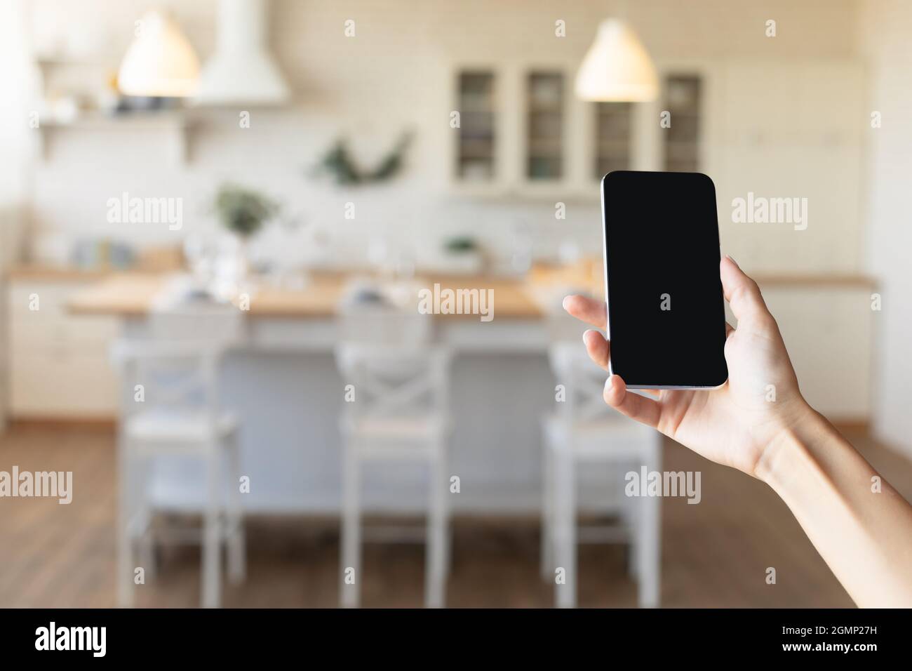 Donna irriconoscibile che tiene il cellulare con mockup per la smart home app o sito web di design interno in sala da pranzo Foto Stock