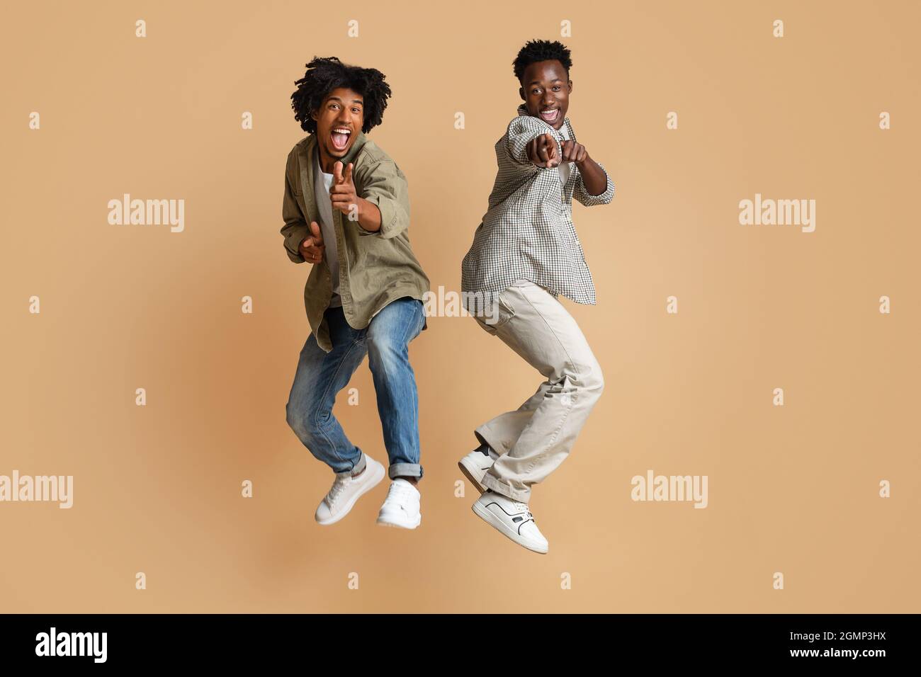 Due allegri ragazzi neri puntano alla fotocamera mentre saltano sullo sfondo di Beige Foto Stock