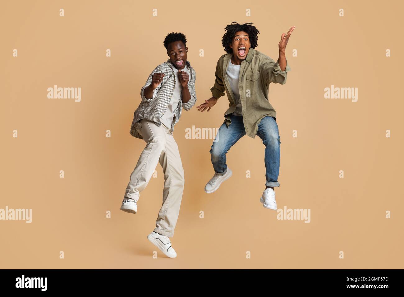 Umore folle. Due allegri Black Guys che saltano sullo sfondo del Beige Studio Foto Stock