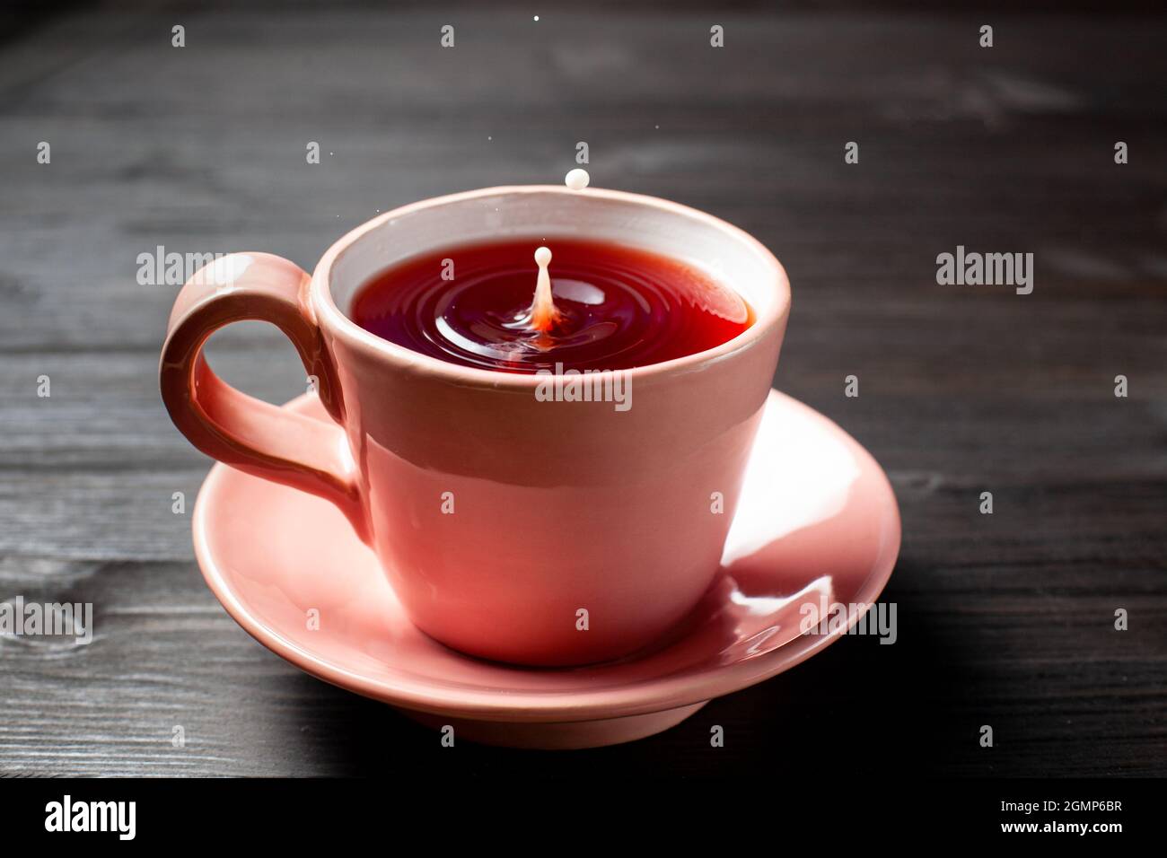 Tazza di tè con una goccia di latte su sfondo di legno Foto stock - Alamy