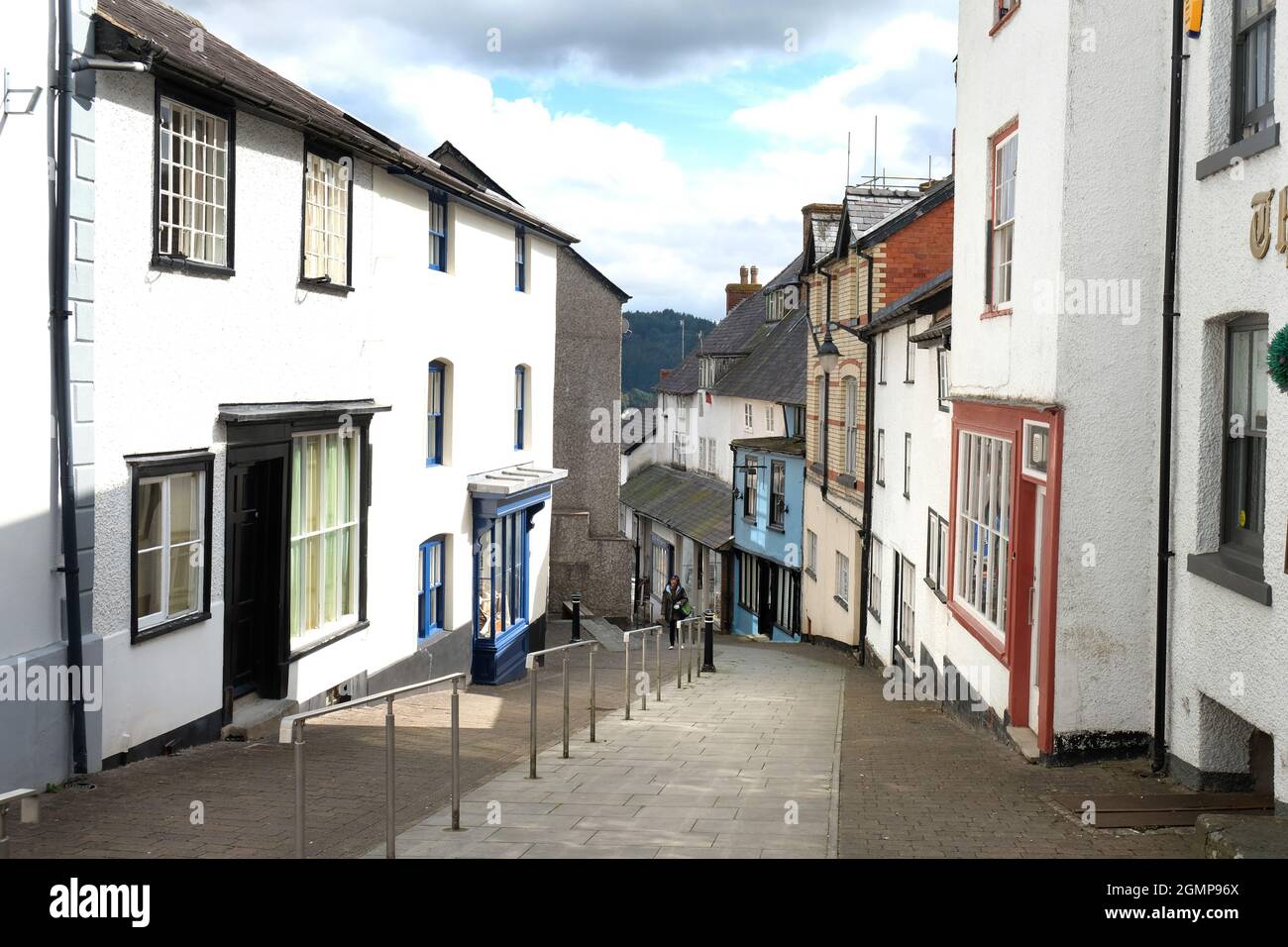 Una donna sale la ripida collina di High Street, Knighton, Powys, Galles. Graziose case a schiera su entrambi i lati della strada Foto Stock