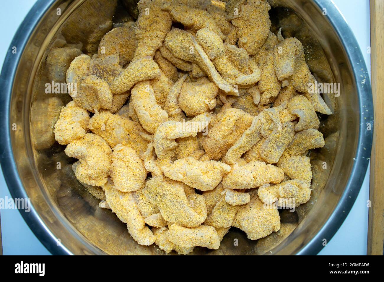 Una ciotola piena di pesce fresco che è stato rivestito in farina di mais e sarà fritto in profondità per una croccante delizia d'oro. Foto Stock