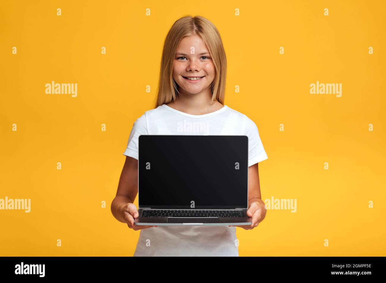 Allegro adolescente bionda ragazza pupilla show laptop con schermo vuoto, isolato su sfondo giallo Foto Stock