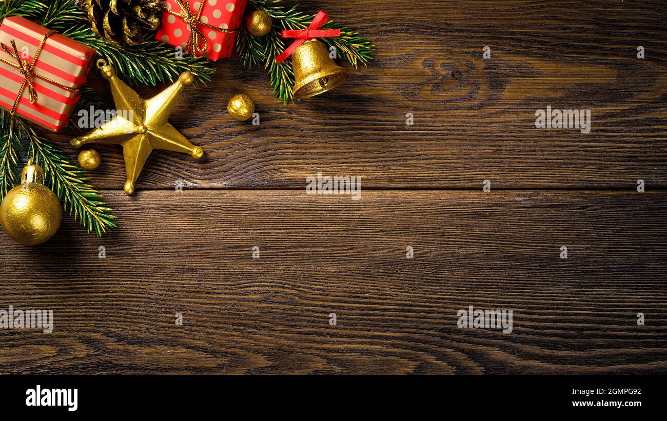 Angolo di Natale con rami di abete pino cono jingle campana e scatole regalo rosse su tavola rustica marrone. Foto Stock