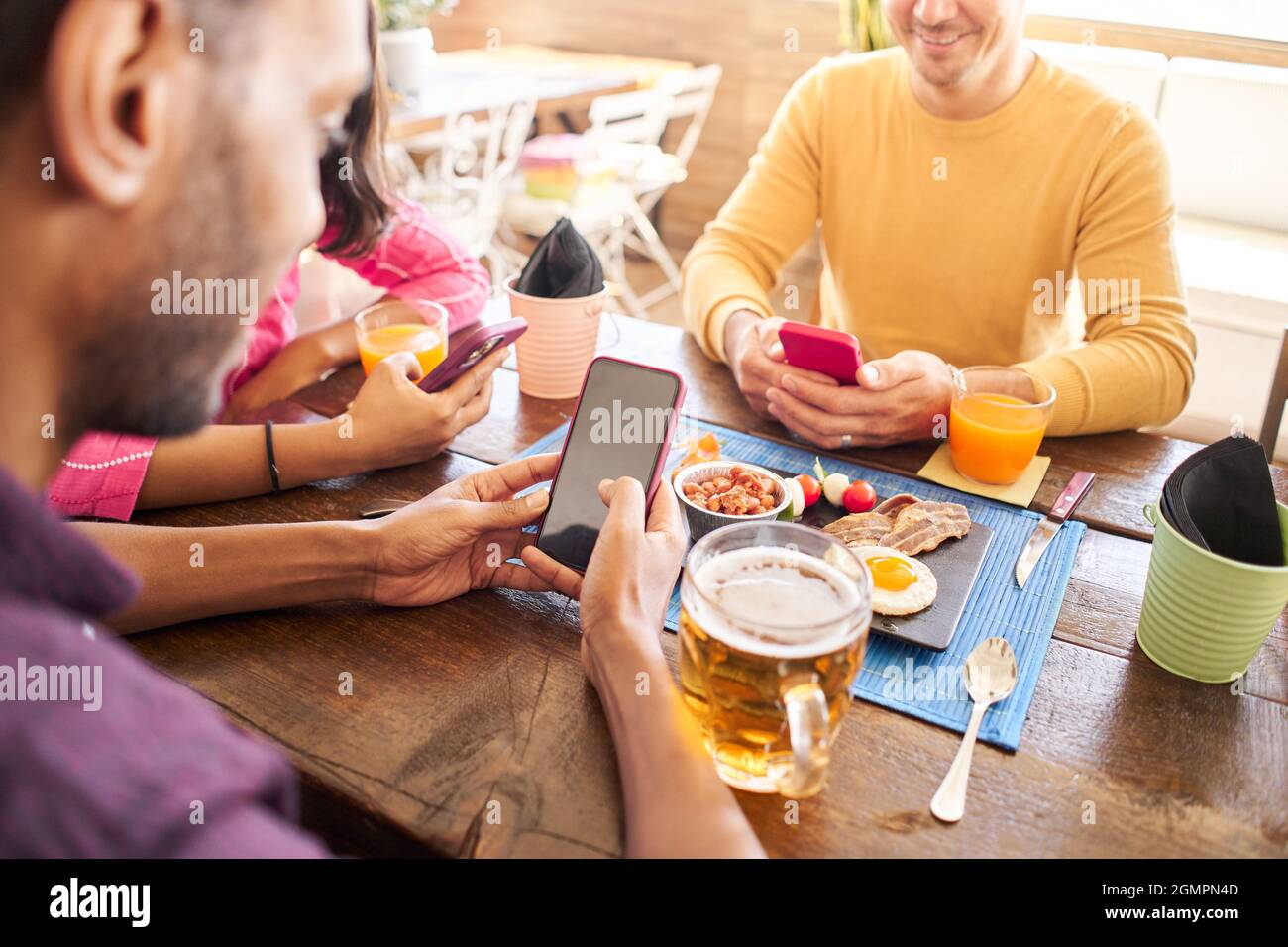 Primo piano di un uomo irriconoscibile utilizzando il suo cellulare in un ristorante, caffè. Gruppo di amici che si divertono a condividere online. Foto Stock