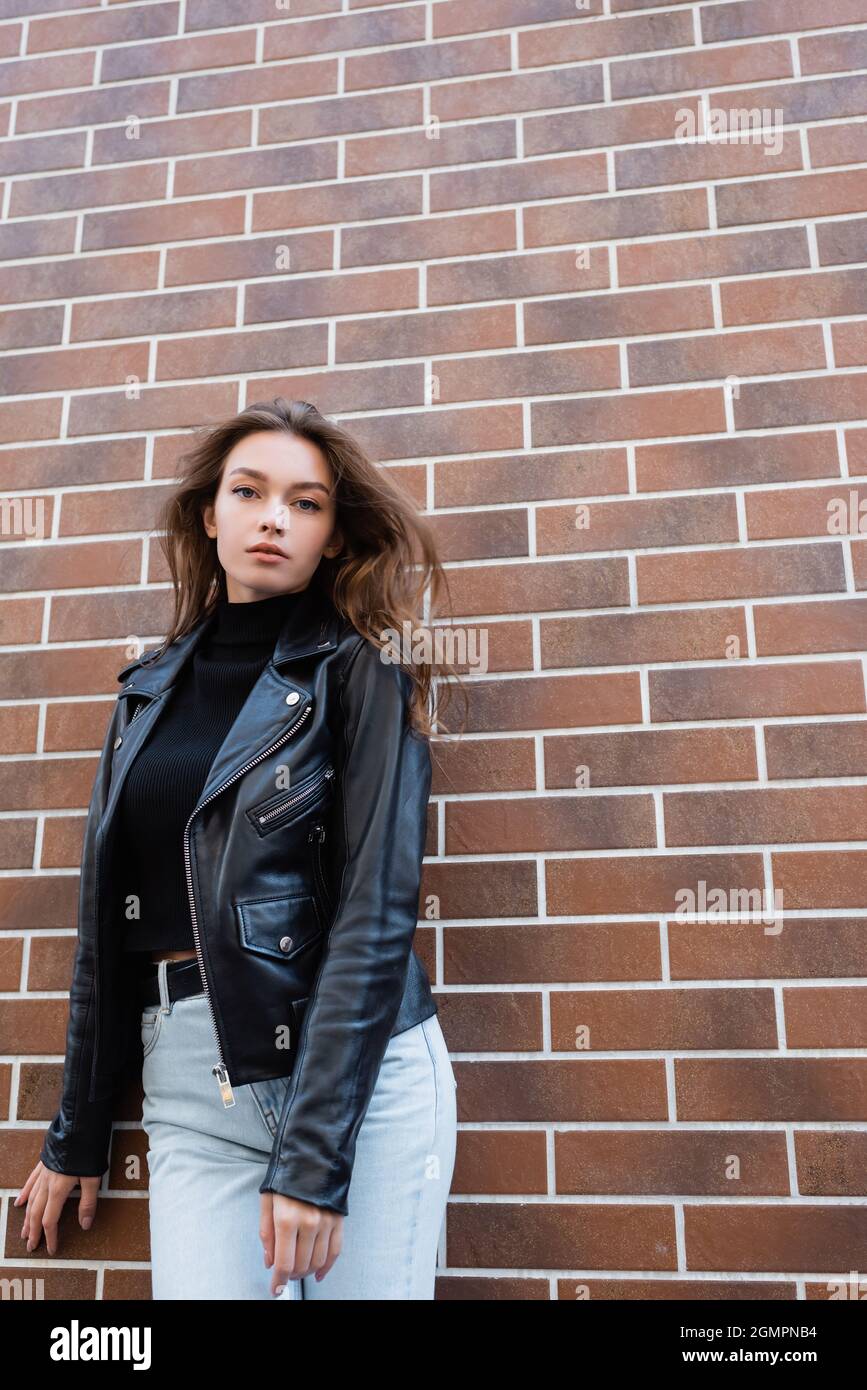 bella giovane donna in giacca di pelle nera e jeans in piedi vicino muro di  mattoni Foto stock - Alamy