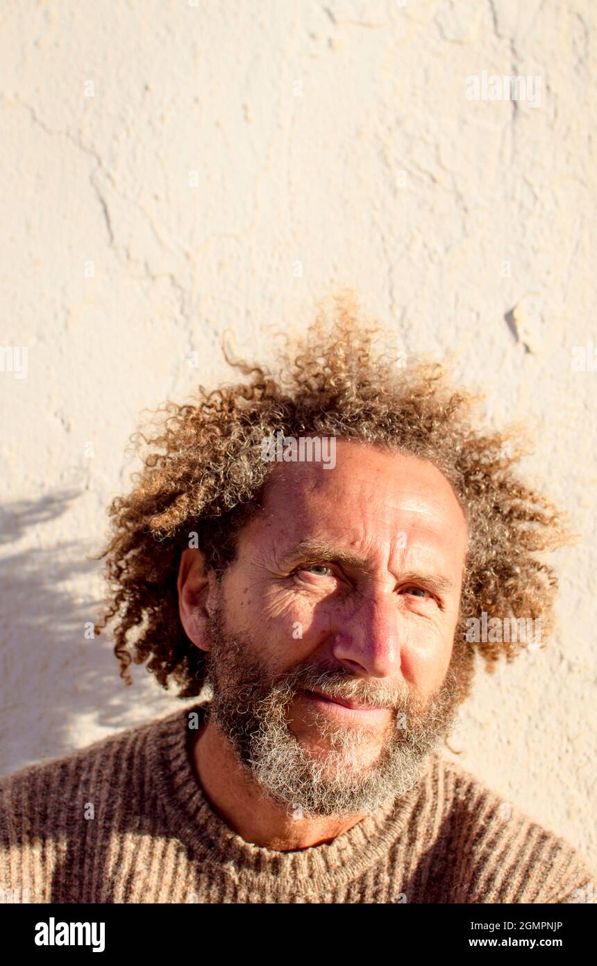 uomo di mezza età con capelli lunghi e naso prominente, è abbagliato dalla luce del sole forte Foto Stock