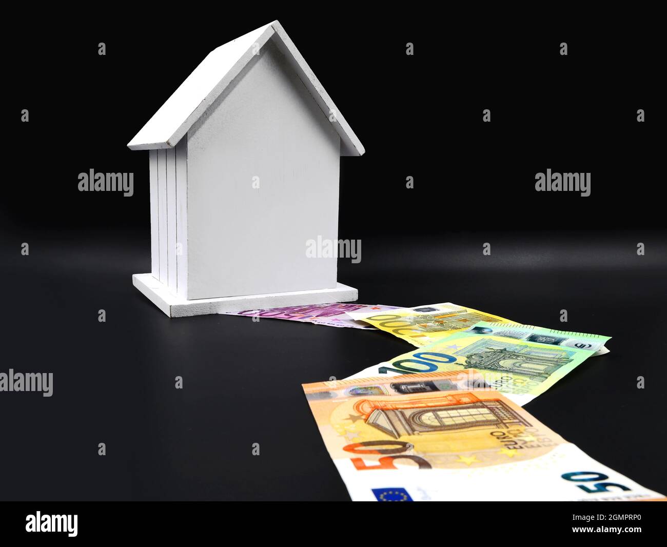 casa in miniatur bianca con percorso delle banconote in euro su sfondo nero, finanza domestica e concetto bancario Foto Stock