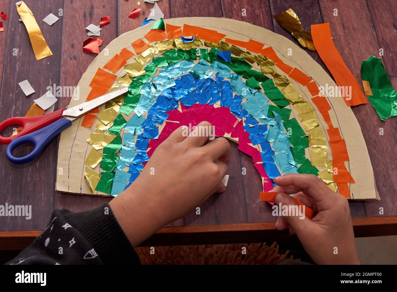 le mani del bambino incollano la carta colorata su un arcobaleno di cartone. compiti della scuola da fare a casa. Orizzontale Foto Stock