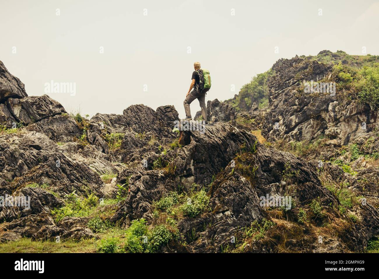 Uomo a piedi con zaino in alto nelle verdi montagne in estate. Osservazione del paesaggio durante una breve pausa. Spazio di copia sul cielo limpido in Vietnam Foto Stock