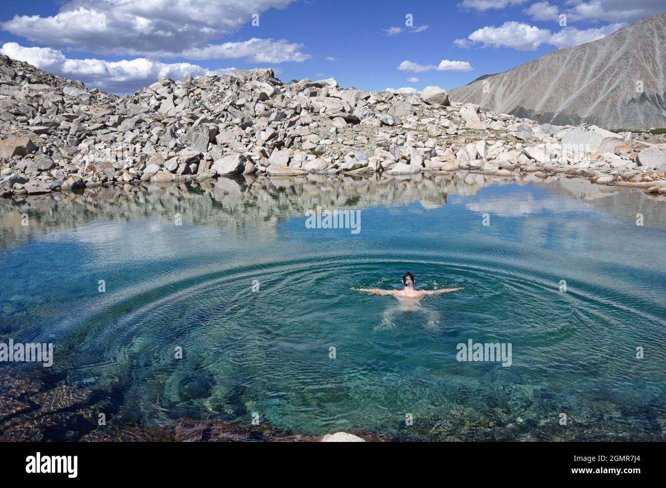 l'uomo nuota in una rinfrescante piscina di montagna blu circondata da rocce Foto Stock