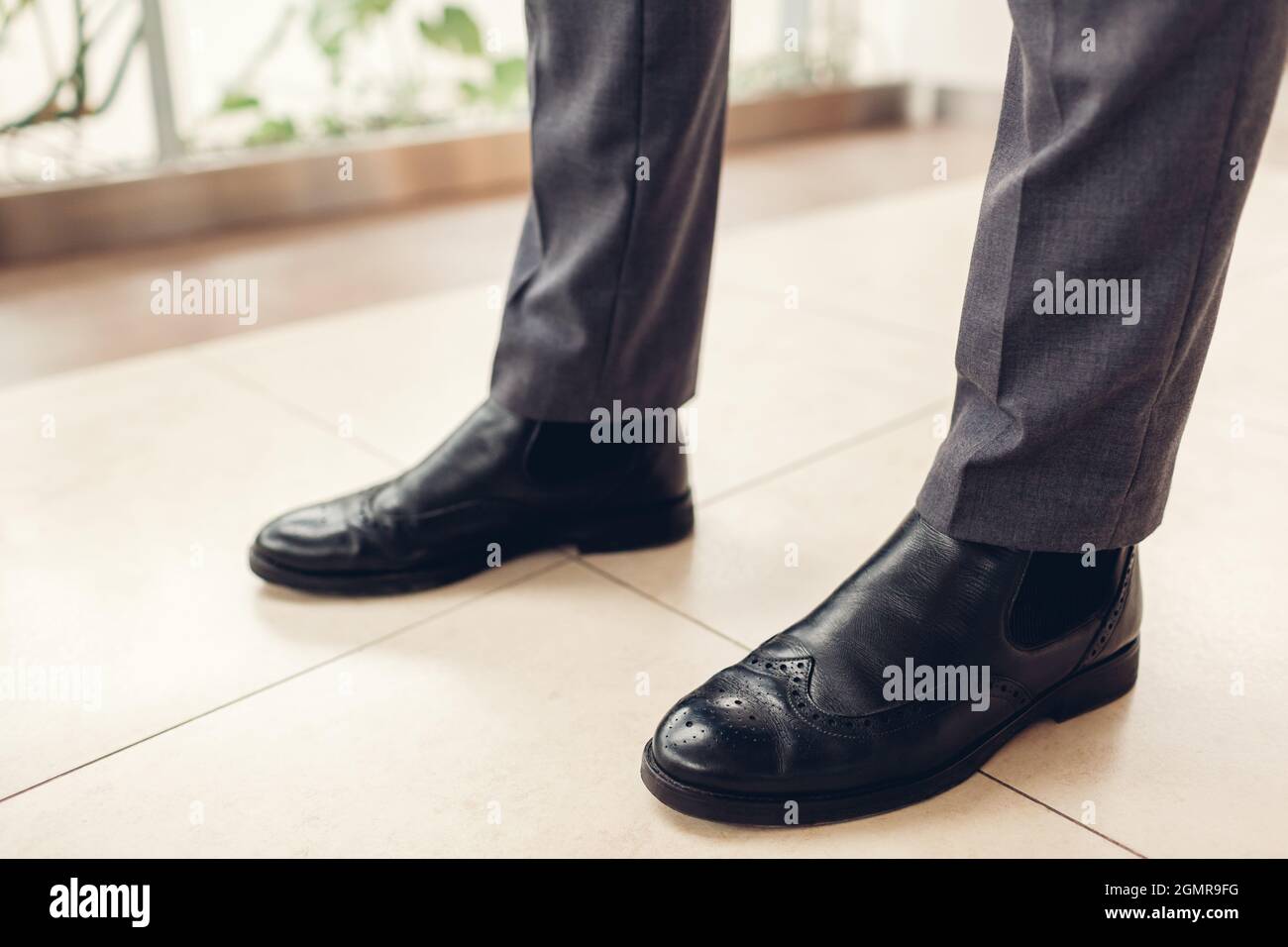 Uomo che indossa stivali chelsea in pelle nera con trafori e pantaloni classici nel centro commerciale. Primo piano dei piedi maschi Foto Stock