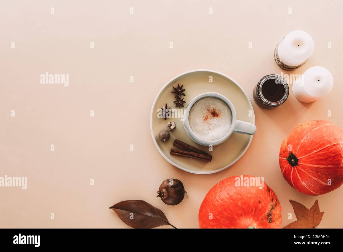 Una tazza di latte di zucca su un piatto con spezie, candele e zucche arancioni hokkaido, foglie autunnali su sfondo di peachy neutro. Vista dall'alto, piatto, c Foto Stock