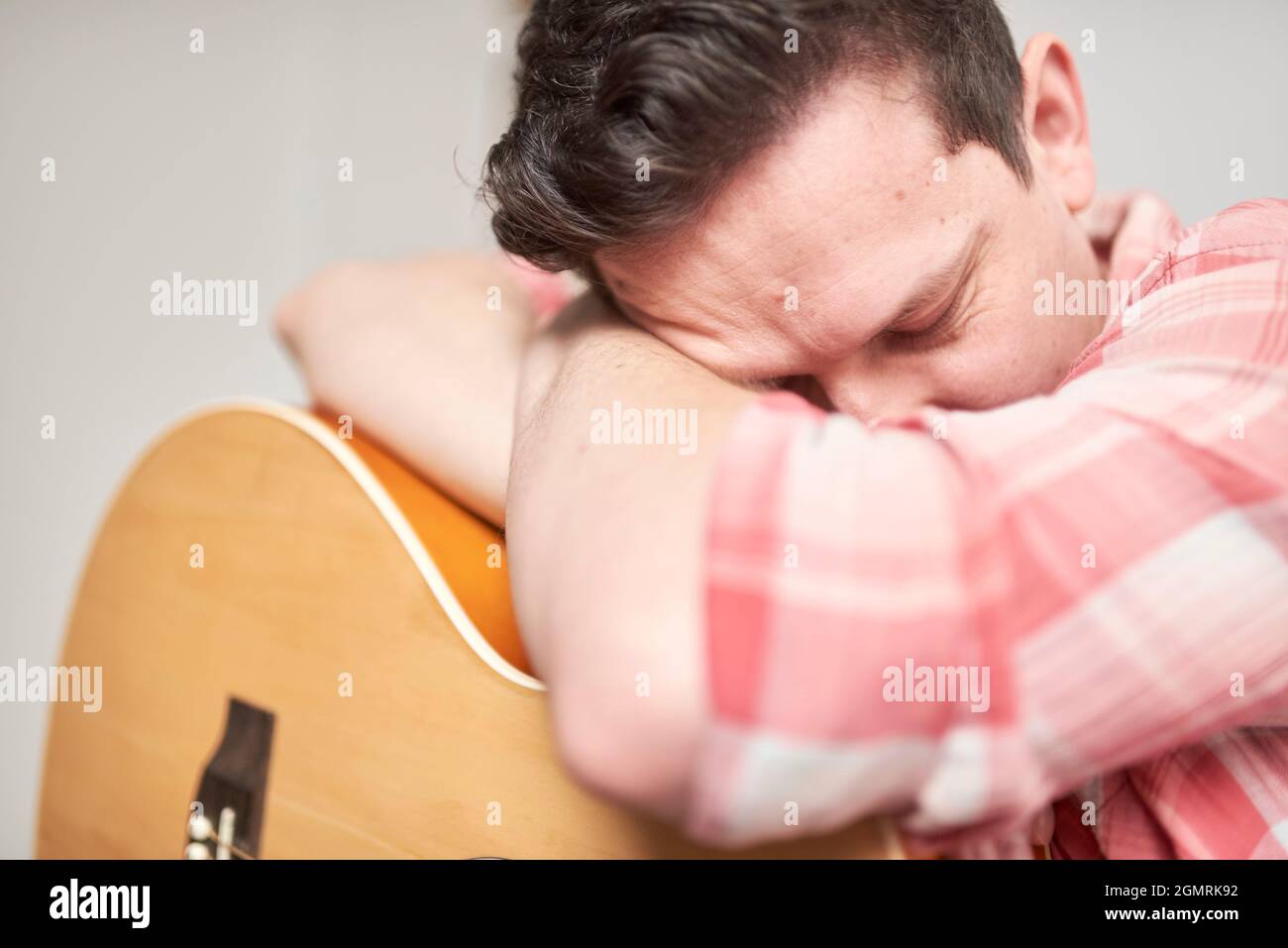 Giovane uomo che riposa sulla sua chitarra acustica, prendendo una pausa dalla riproduzione dello strumento. Foto Stock