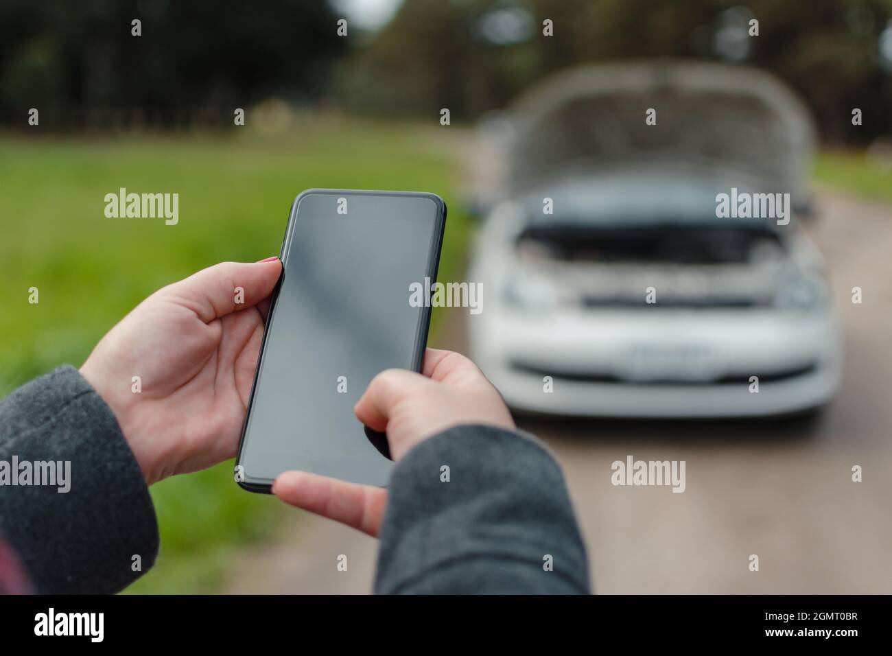 Primo piano delle mani di una donna utilizzando un telefono cellulare per chiamare aiuto con la sua auto rotta Foto Stock