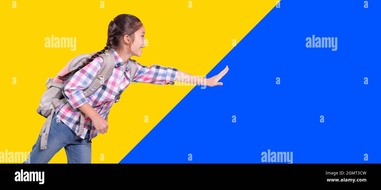 Ragazza felice studente con borsa scuola. Correre e toccare qualcosa. Isolato su sfondo giallo e blu. Foto Stock