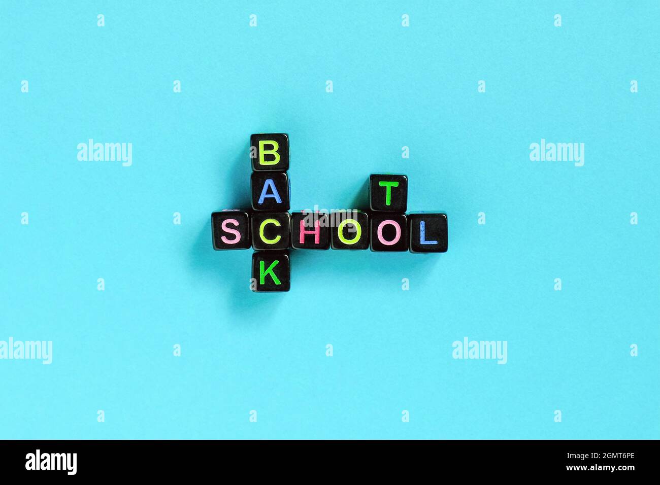 Testo di ritorno a scuola da lettere colorate su cubi neri disposti in forma di puzzle cruciverba, sfondo blu. Formazione concettuale e inizio di sch Foto Stock