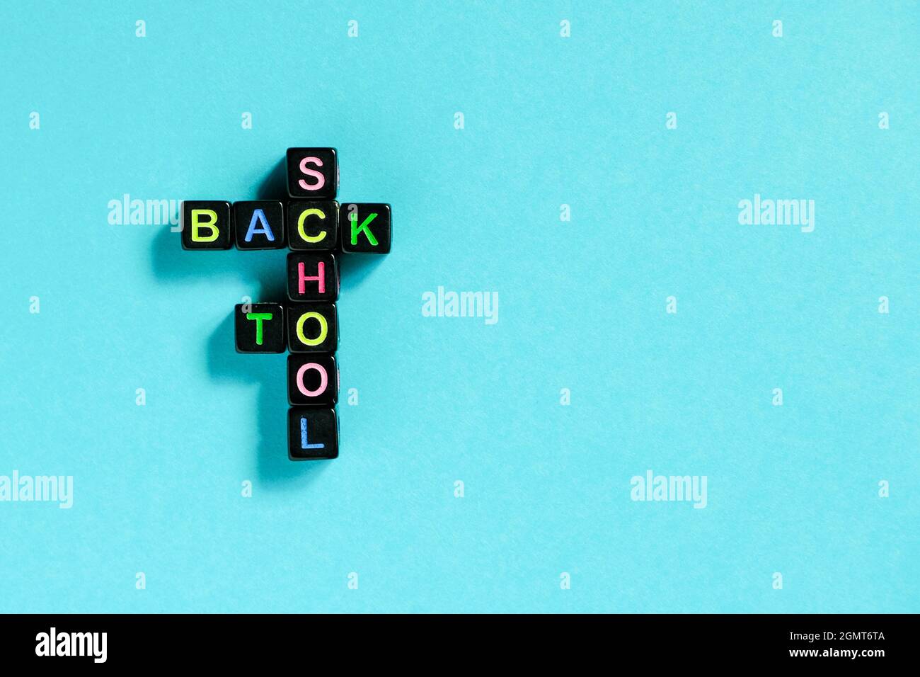Testo di ritorno a scuola da lettere colorate su cubi neri disposti in forma di puzzle cruciverba, sfondo blu. Formazione concettuale e inizio di sch Foto Stock