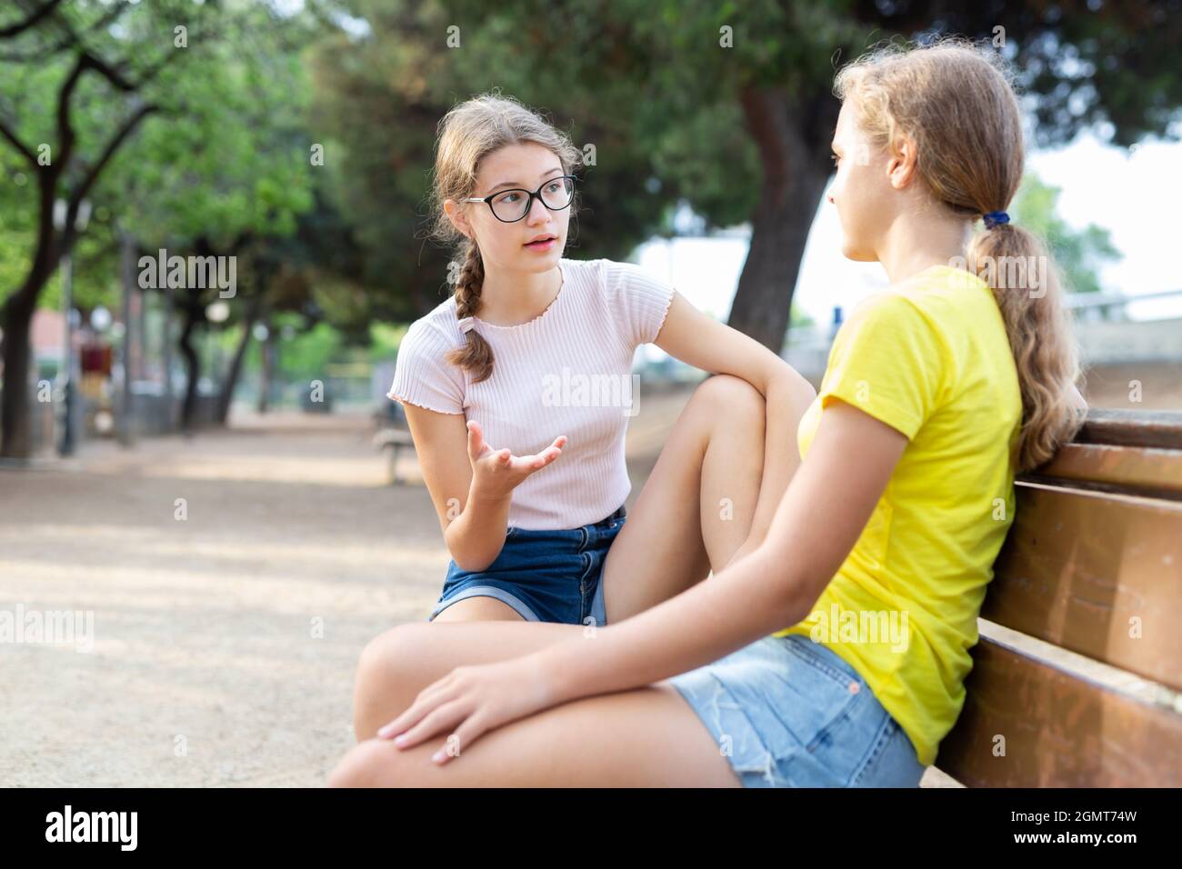Ragazze giovani in pantaloncini seduti su panca Foto Stock