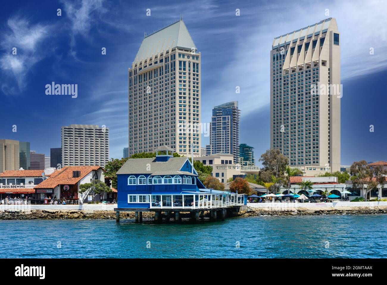 Il ristorante del Molo di San Diego in stile retrò blu e bianco su palafitte nel Seaport Village, con alti edifici incombenti sulla baia di San Diego, CA Foto Stock