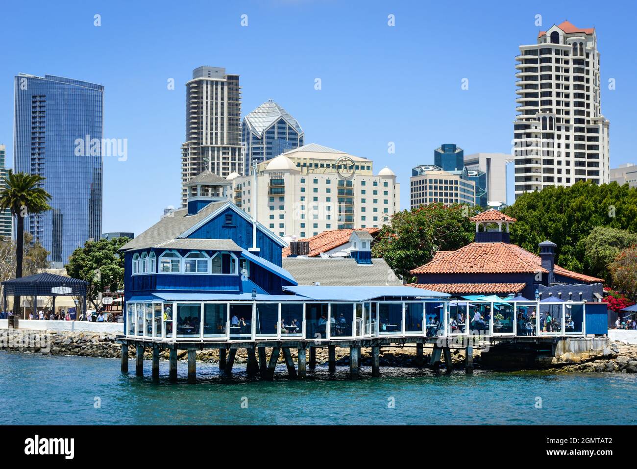 Il ristorante del Molo di San Diego in stile retrò blu e bianco su palafitte nel Seaport Village, con alti edifici incombenti sulla baia di San Diego, CA Foto Stock