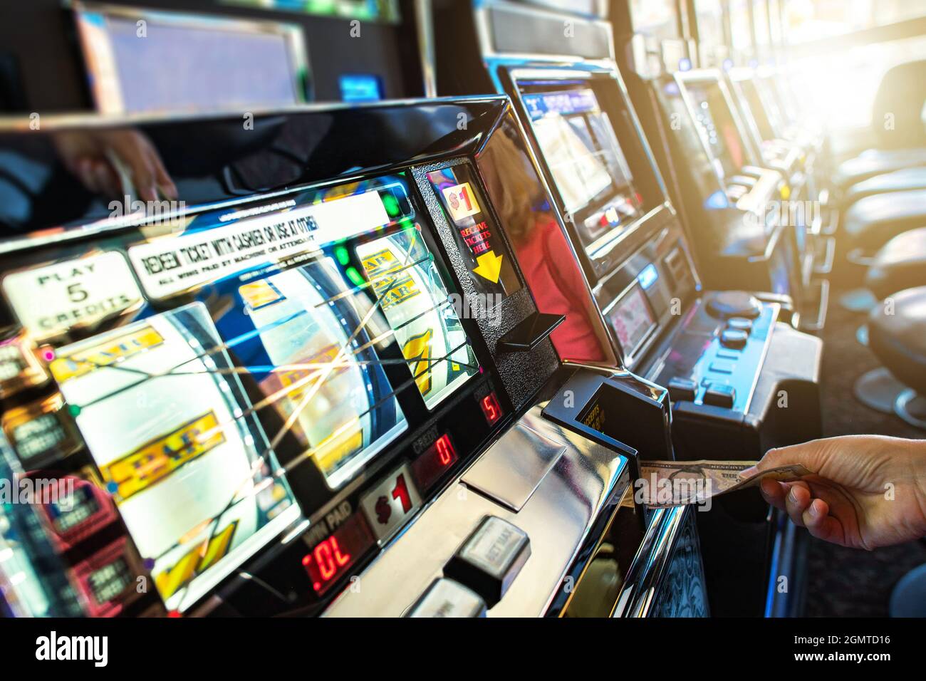 Slot Machine di Las Vegas giocatore caucasico che inserisce la banconota per un altro gioco di Bandit con una mano. Gioco d'azzardo industria tema. Foto Stock