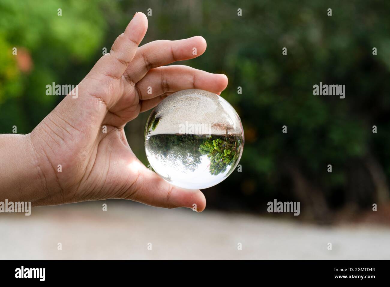 Mano che tiene una sfera di cristallo trasparente con una vista capovolta di un paesaggio. Sfondo sfocato Foto Stock