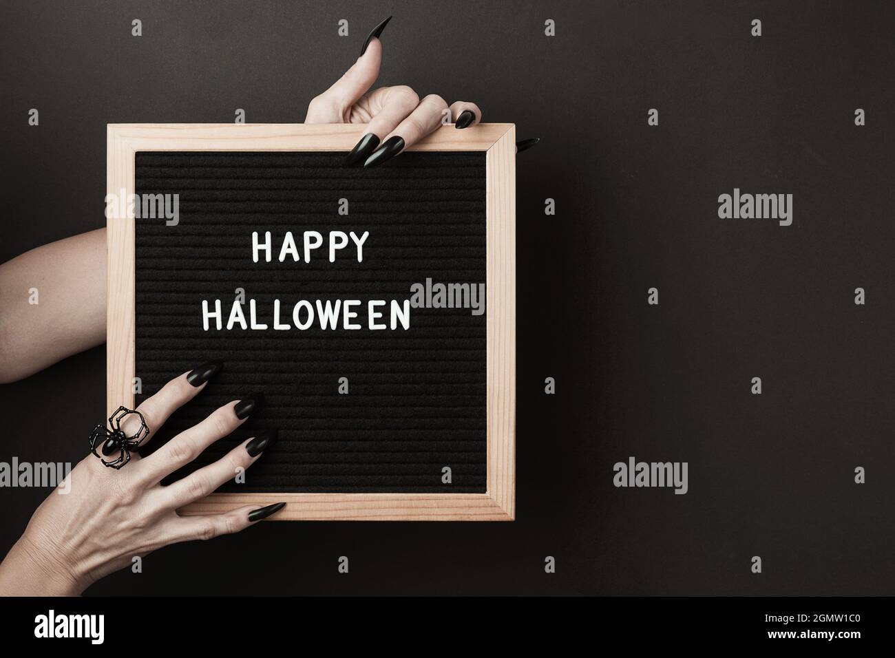 Halloween felice sulla scheda della lettera in mani con le unghie nere lunghe e l'anello del ragno su sfondo nero. Halloween concetto di vacanza. Foto Stock