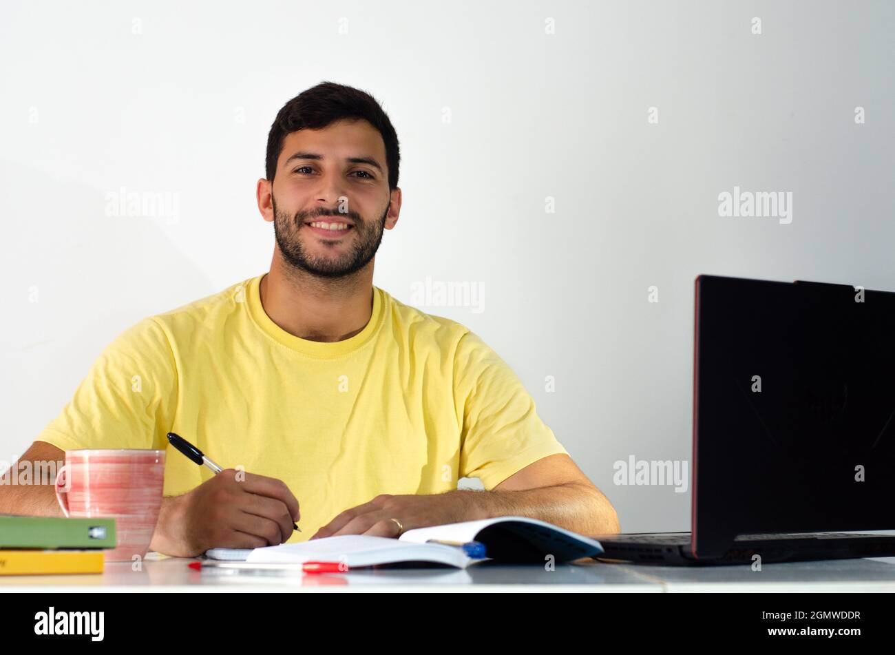 Ritratto di studente concentrato che si prepara per l'esame a casa. Studente adulto che prende appunti nel suo libro mentre guarda una classe virtuale. Uomo d'affari writ Foto Stock