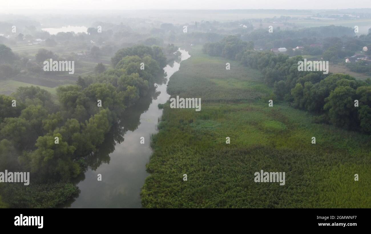 Mattina nebbia su un prato pianura e fiume alluvione vicino a un villaggio rurale con una casa. Paesaggio rurale nella valle da un'altezza di volo Foto Stock