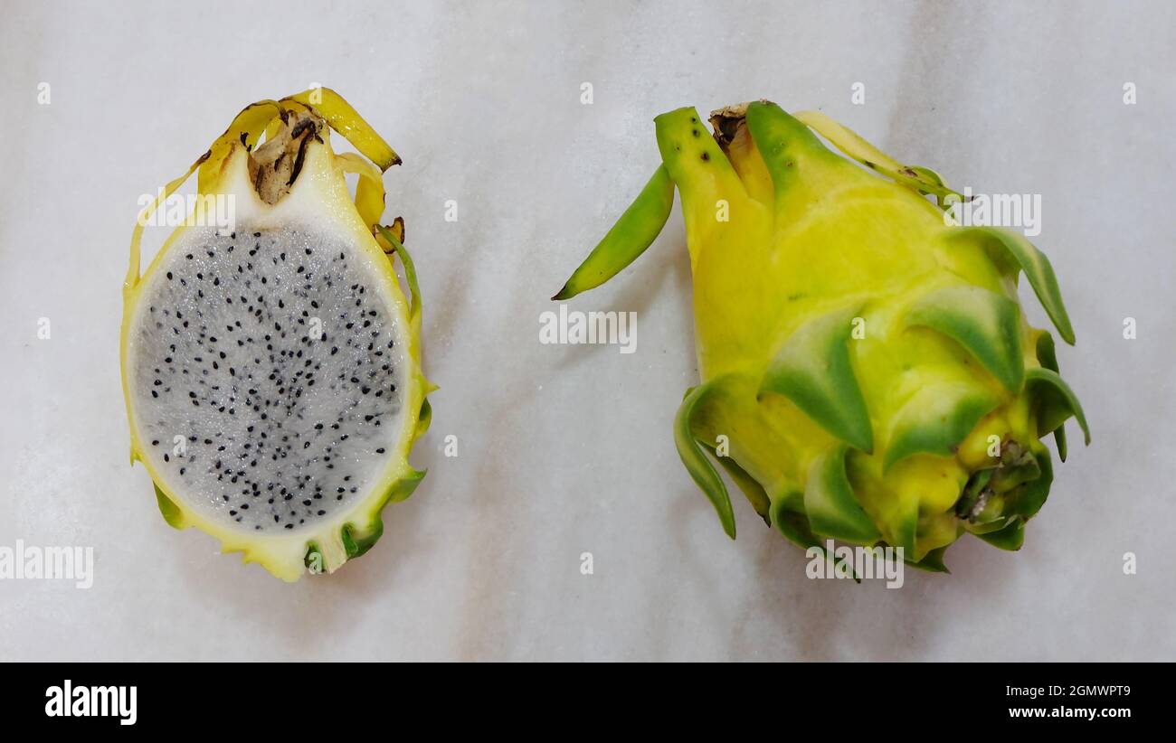 Vista dall'alto di due frutti di drago gialli. Uno con la pelle, l'altro tagliato a metà con la carne all'interno esposta. Foto Stock