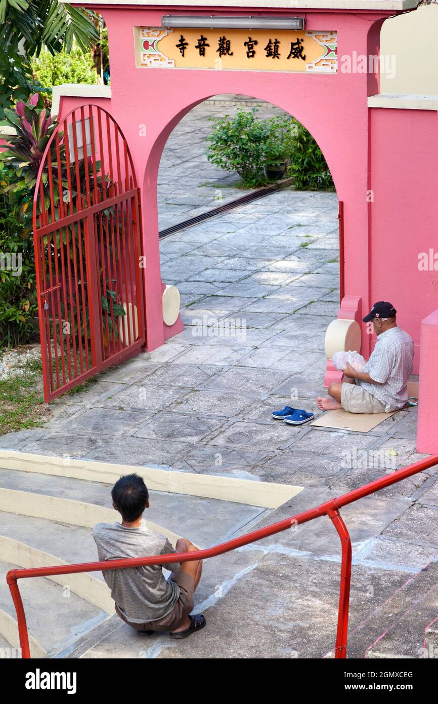 Kuala Lumpur, Malesia - 3 aprile 2011, due vecchi uomini seduti in vista. Proprio accanto alla linea della monorotaia, questo piccolo e scioccante tempio Daoista rosa richiede Foto Stock