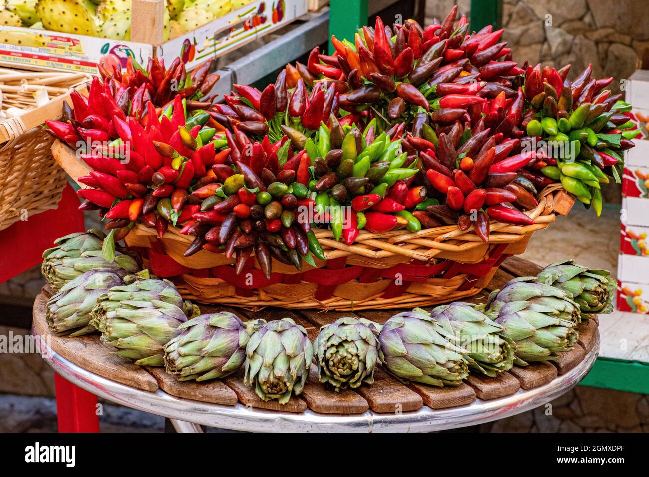 Carciofi verdi freschi con foglie verdi e mazzi di peperoncini rossi e verdi in un cestino in un mercato di Street food Foto Stock